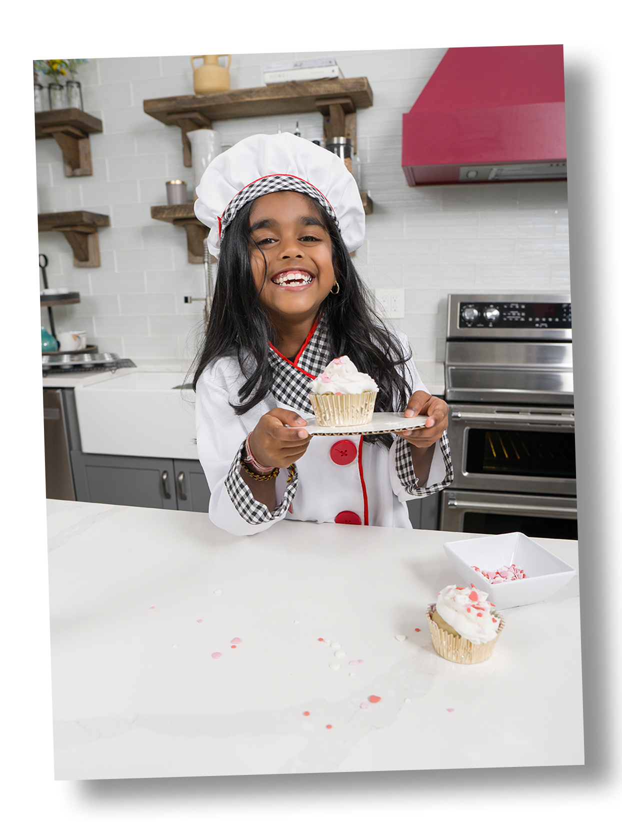 Sira Garib's daughter Kaliya holding one cupcakes, smiling in a kitchen